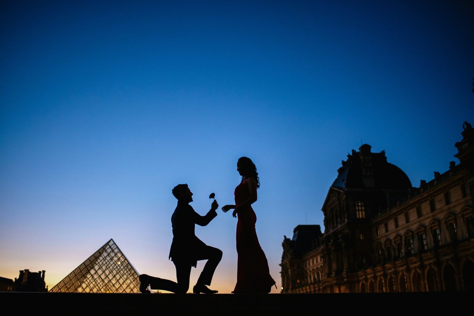 a man kneeling down next to a woman in front of a pyramid